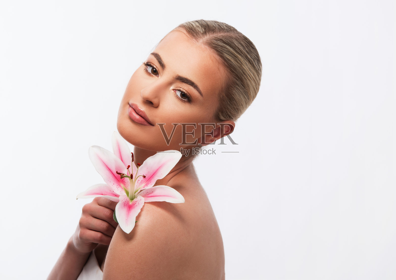 一个美丽的女人举着一朵美丽的粉红色百合花在白色的背景上照片摄影图片