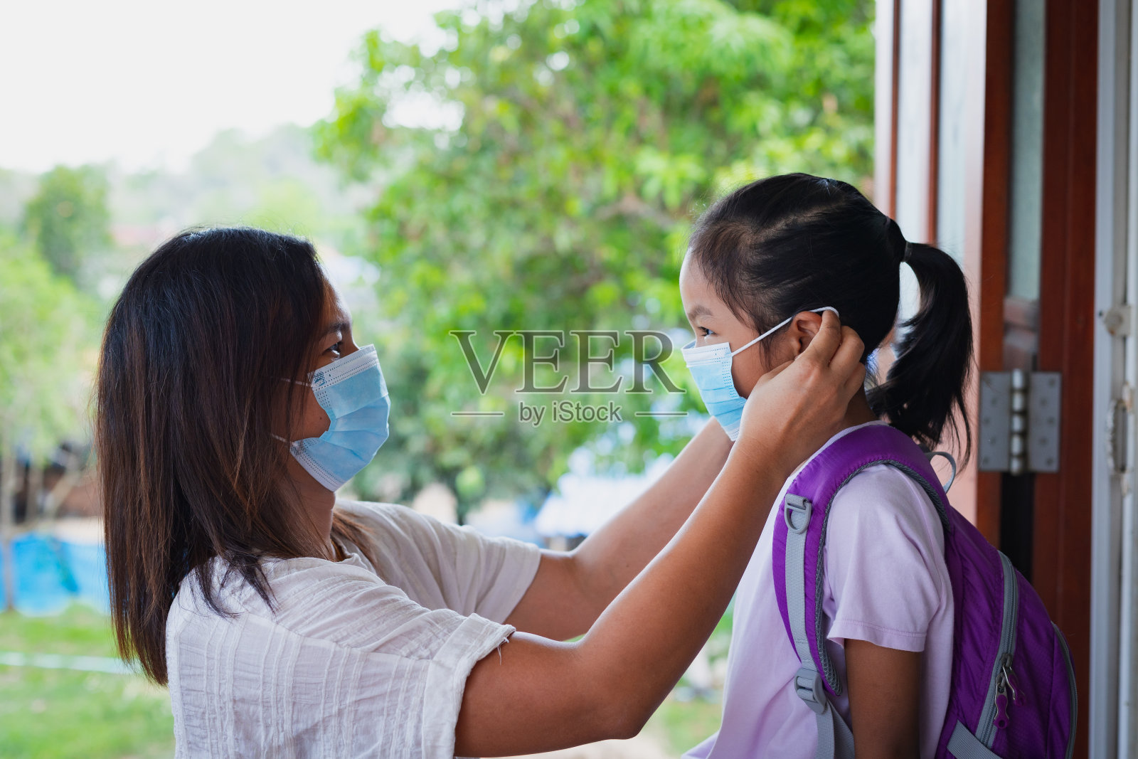 亚洲母亲在外出前帮助女儿佩戴医用口罩，作为新冠肺炎疫情新常态的生活方式。照片摄影图片
