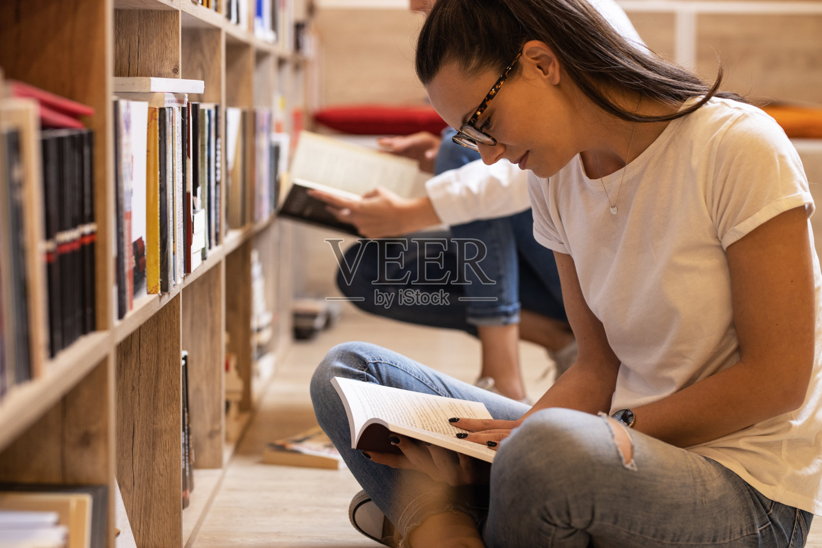 年轻女学生在图书馆的书架上阅读和学习。阅读一本书。照片摄影图片