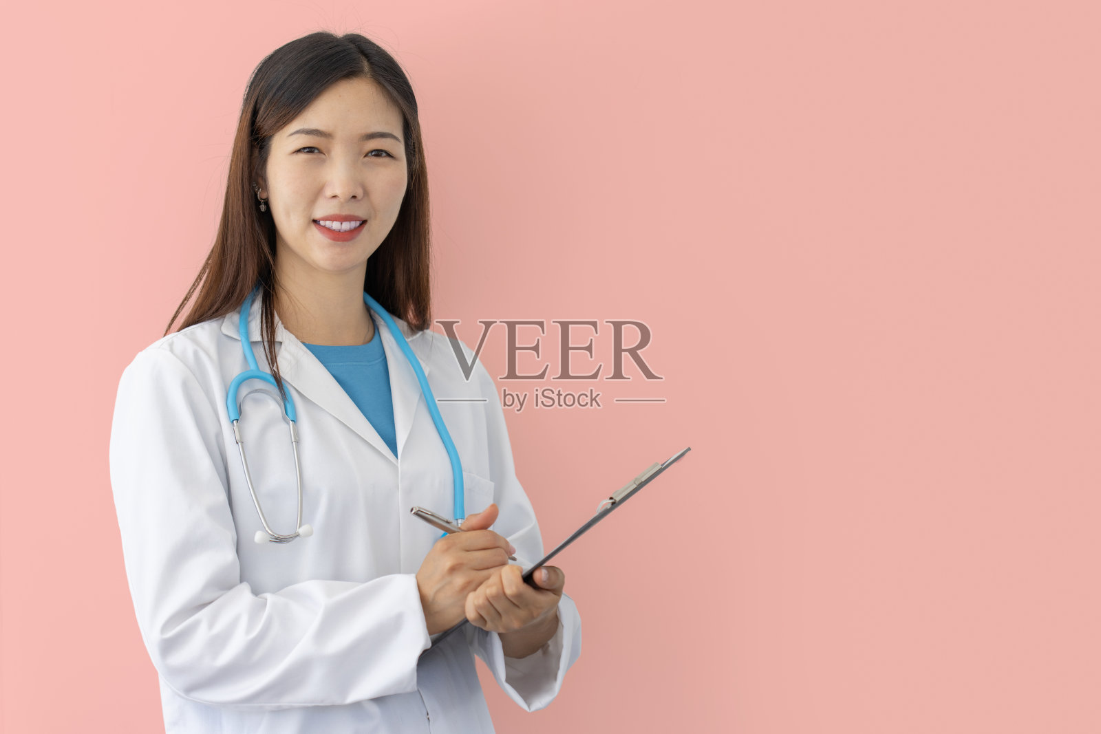 微笑的女医生在粉红色的背景与实验室大衣和听诊器持有医疗文件夹在手里照片摄影图片