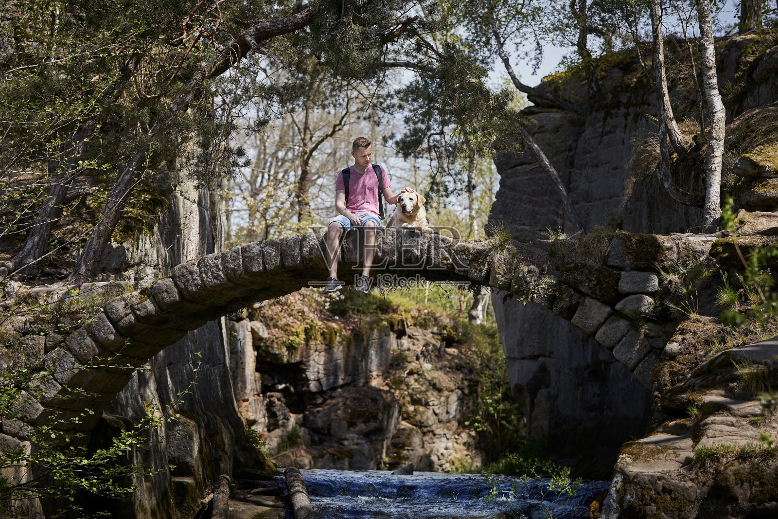 一个人和他的狗坐在美丽的自然中古老的石桥上照片摄影图片