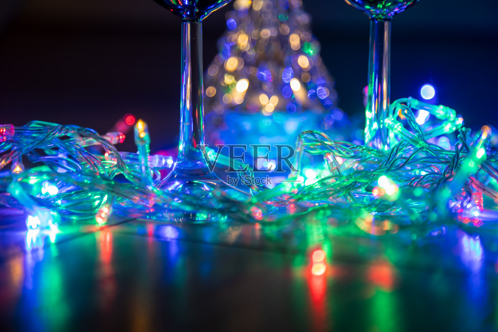 两个玻璃杯在一个明亮的圣诞树的背景和一个多色的花环在黑暗的背景。新年的庆祝活动。照片摄影图片