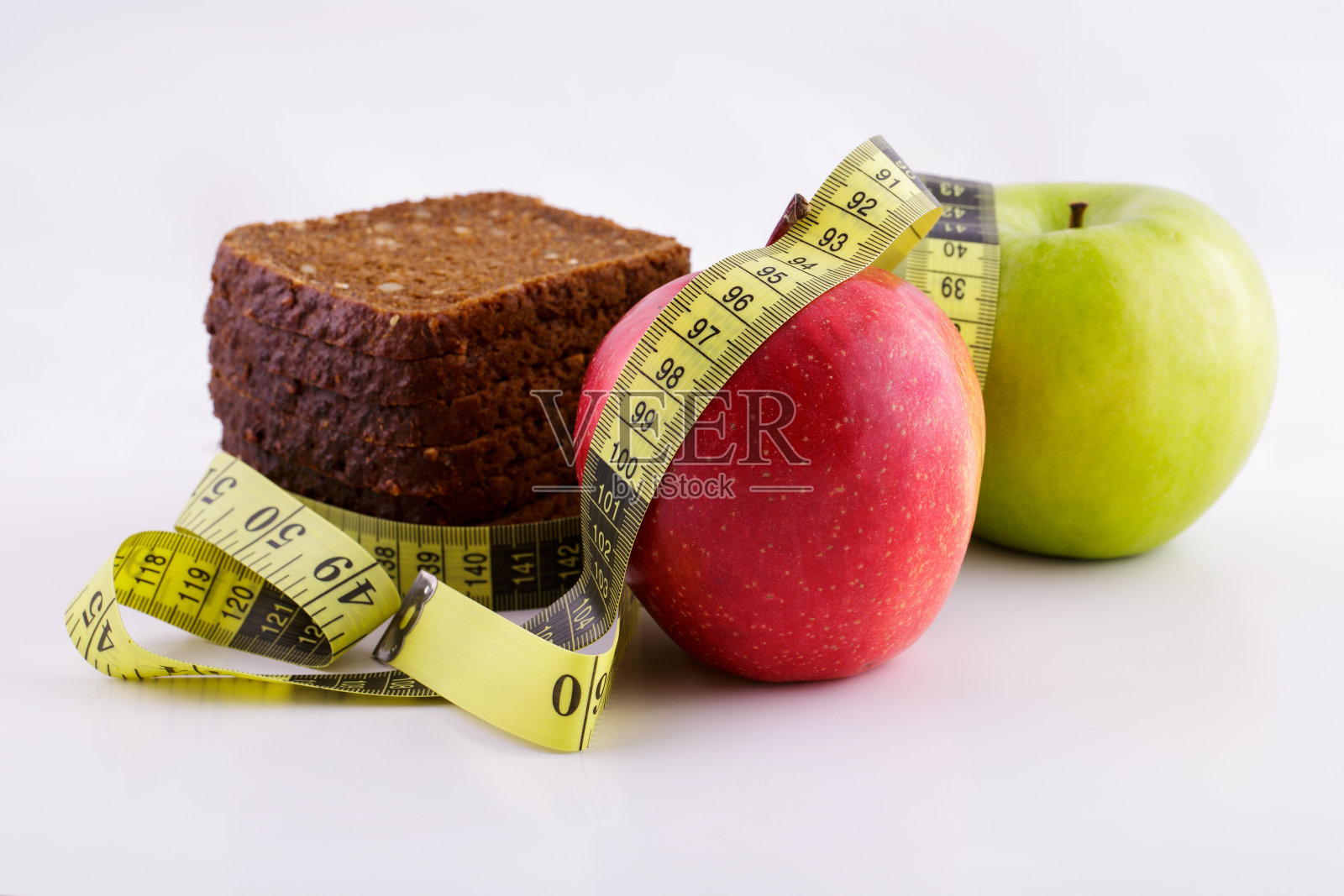 黑色的切片面包和绿色和红色的苹果躺在白色的背景与黄色的卷尺，饮食概念照片摄影图片