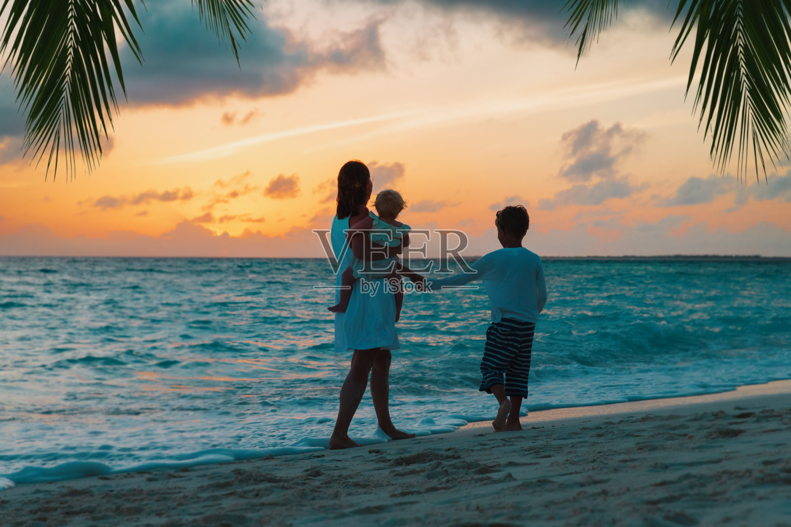 母亲和两个孩子在日落海滩散步照片摄影图片