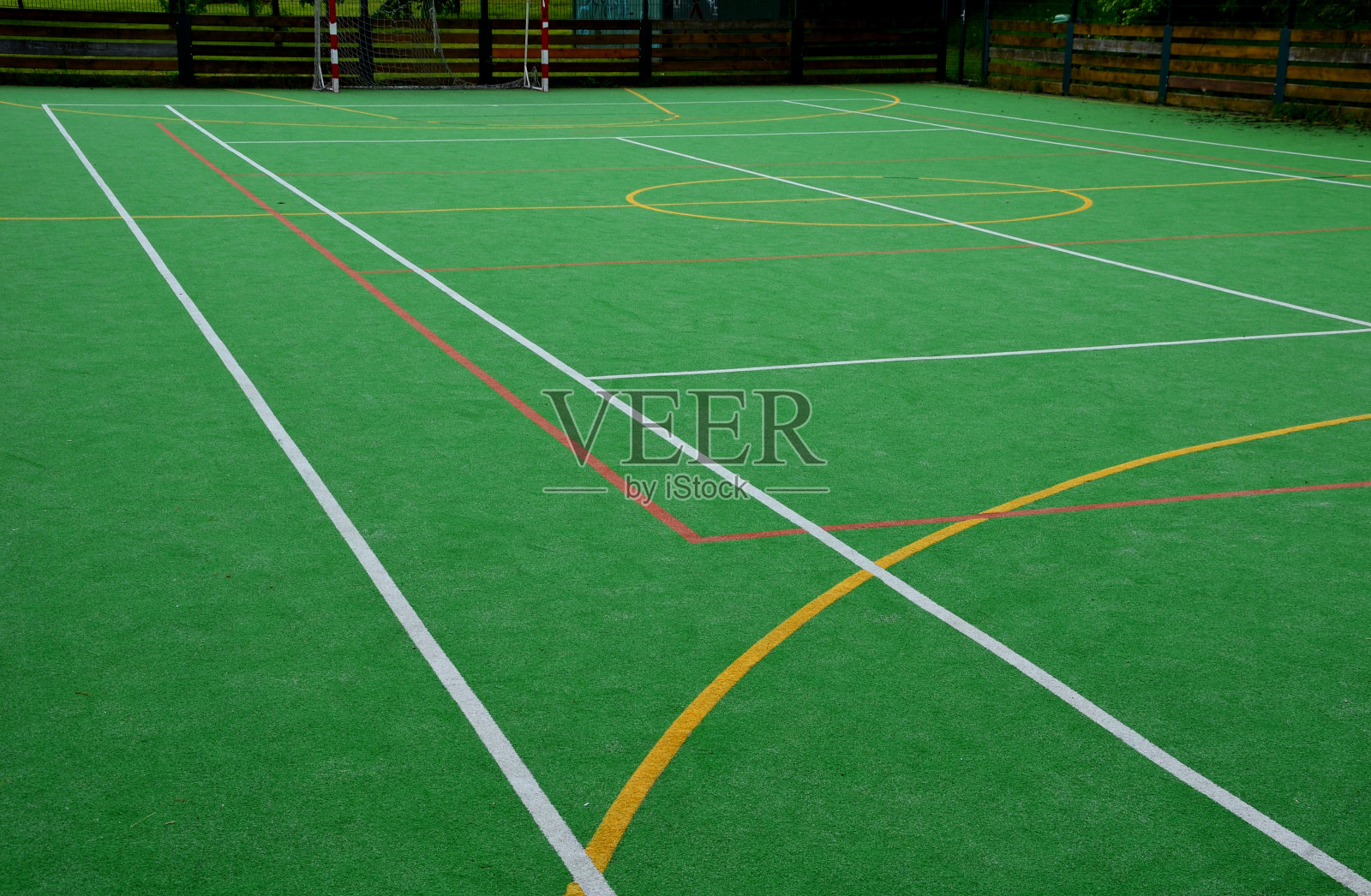 学校多功能户外球类运动场地。有线条的塑料地毯上的绿色人造草皮。篮球篮筐和足球球门。围绕着高高的网和护栏照片摄影图片