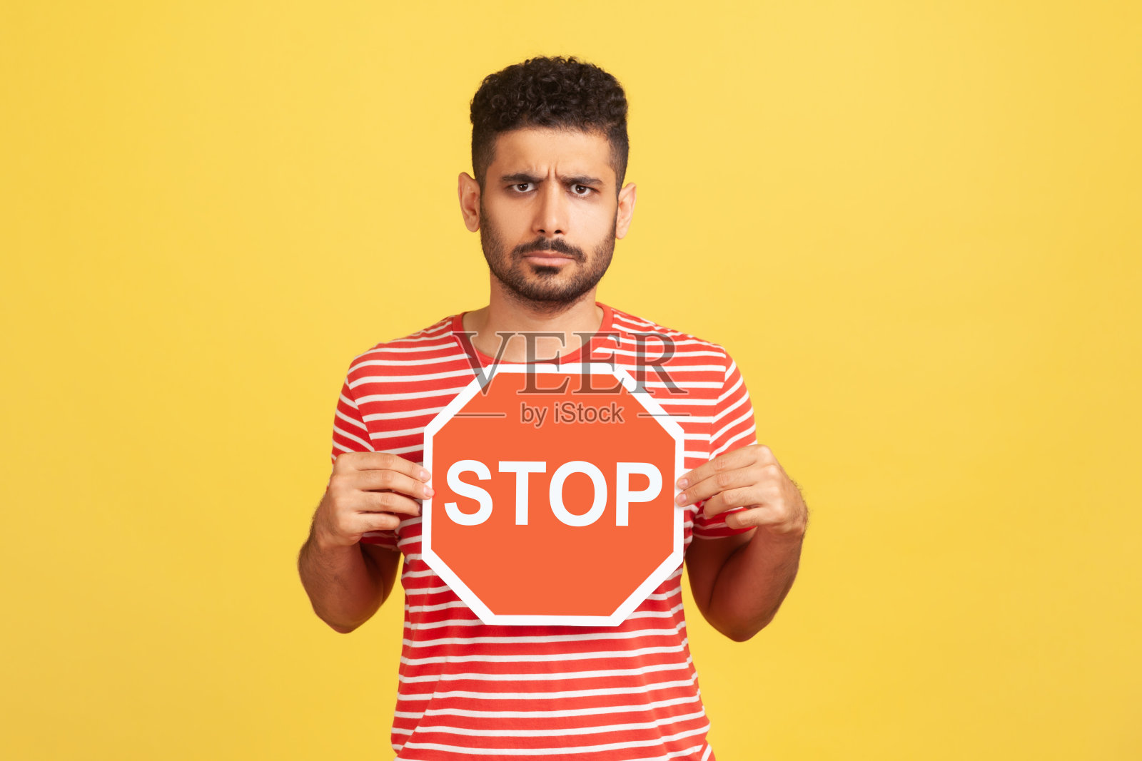 关切愤怒的男子胡子条纹t恤拿着红色停止交通标志，警告限速，危险的道路照片摄影图片