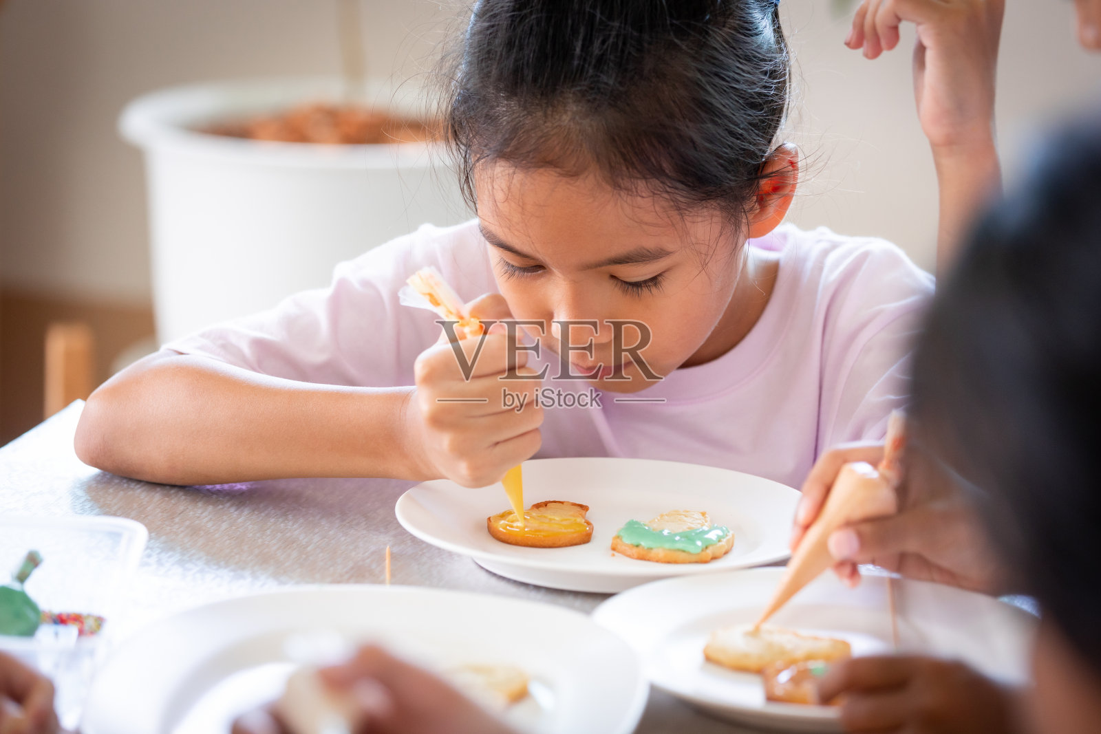 近距离的亚洲小女孩挤冰淇淋装饰饼干与朋友与乐趣。照片摄影图片
