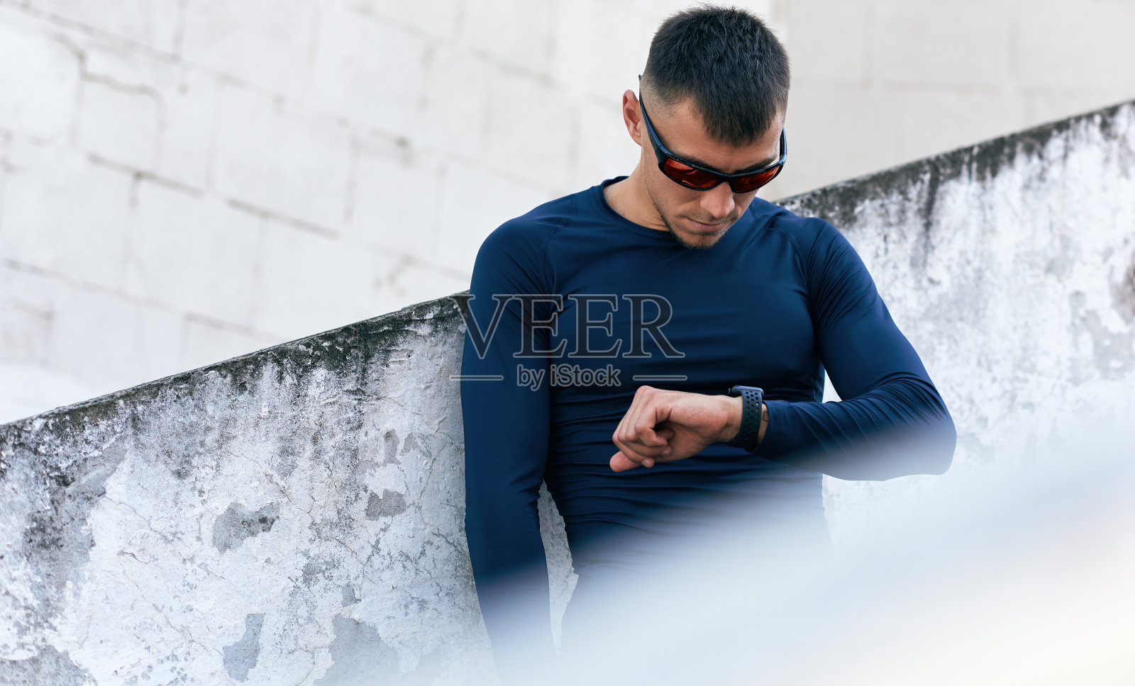 运动健将穿着时尚运动服，在户外运动前看智能手表。健身男子在城市街道跑步前准备。照片摄影图片