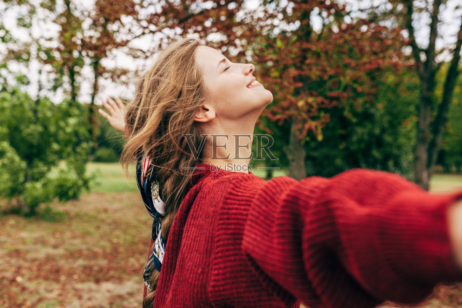 一个真实的年轻女子微笑着双臂张开在自然背景摆姿势的水平图像。快乐的女性享受在公园的时间。心理健康的概念照片摄影图片