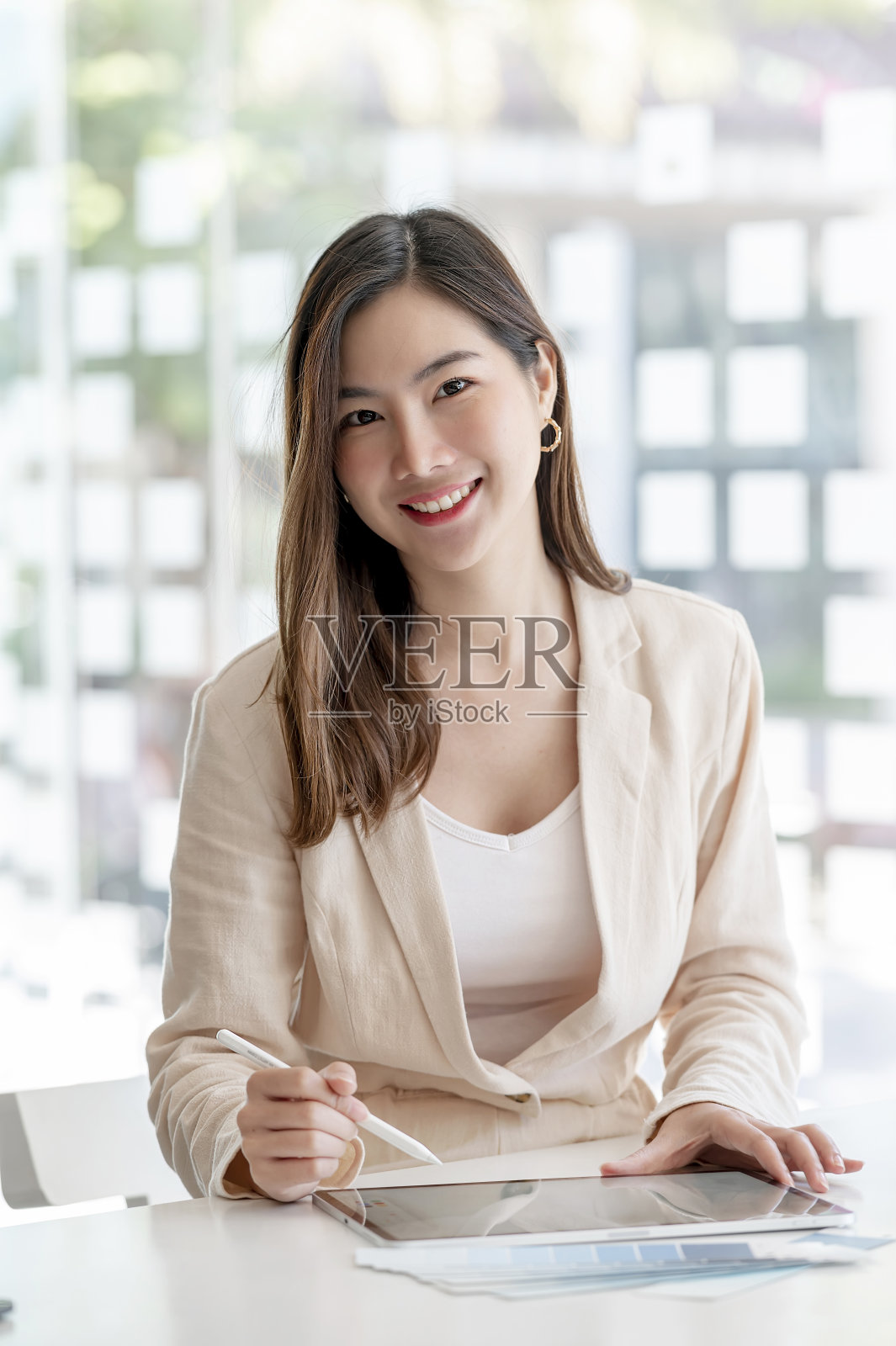 年轻美丽的亚洲女人的肖像，微笑着看着相机，而在办公室工作。照片摄影图片