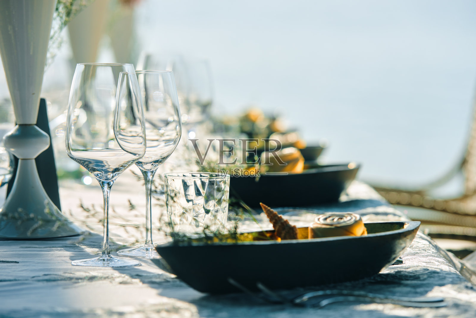 节日餐桌装饰，酒杯和桌子设置在海滩上。专注于用酒杯做的菜照片摄影图片
