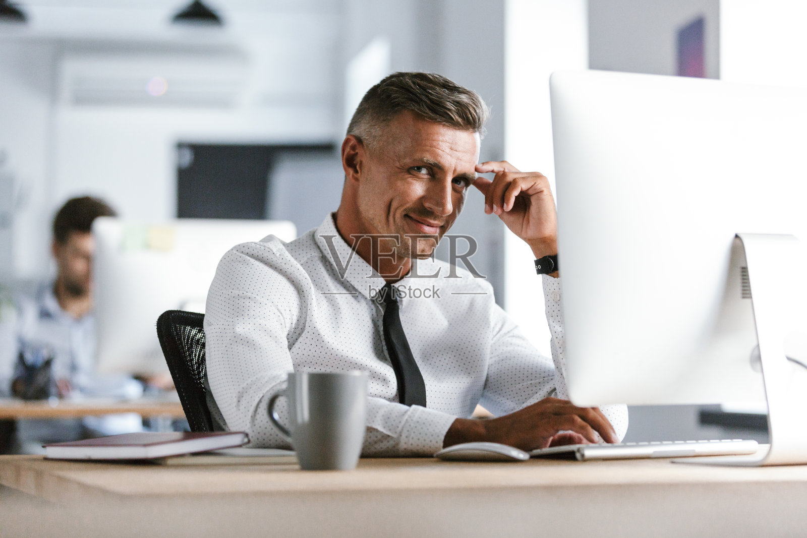 一幅30多岁的欧洲商人的肖像，穿着白衬衫，打着领带坐在办公室的办公桌前，在电脑前工作照片摄影图片