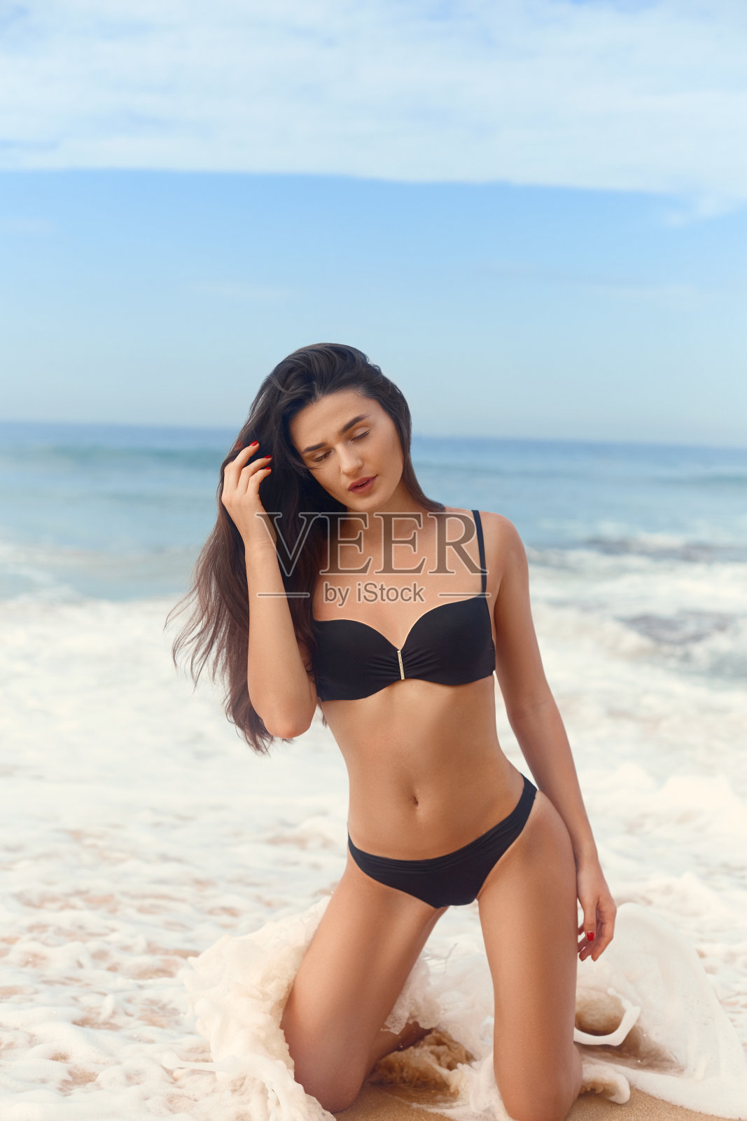 美丽的豪华苗条的女孩穿着黑色比基尼在海滩上的海洋。美丽的女人性感的古铜色身体，平坦的腹部，完美的身材。在一个热带岛屿上休息。照片摄影图片