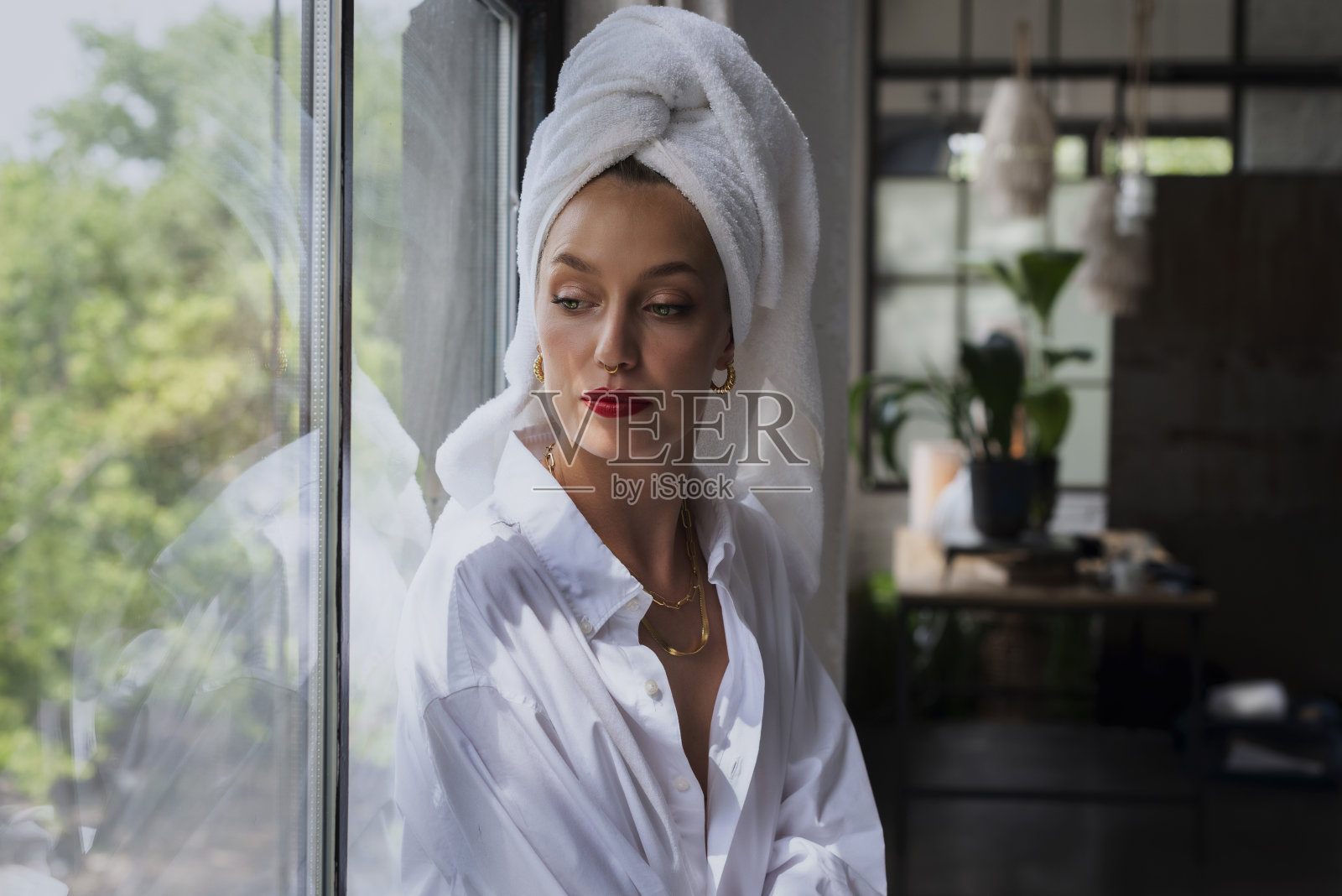 一幅美丽女子的肖像，身穿白衬衫，头戴头巾，坐在窗前做着白日梦照片摄影图片