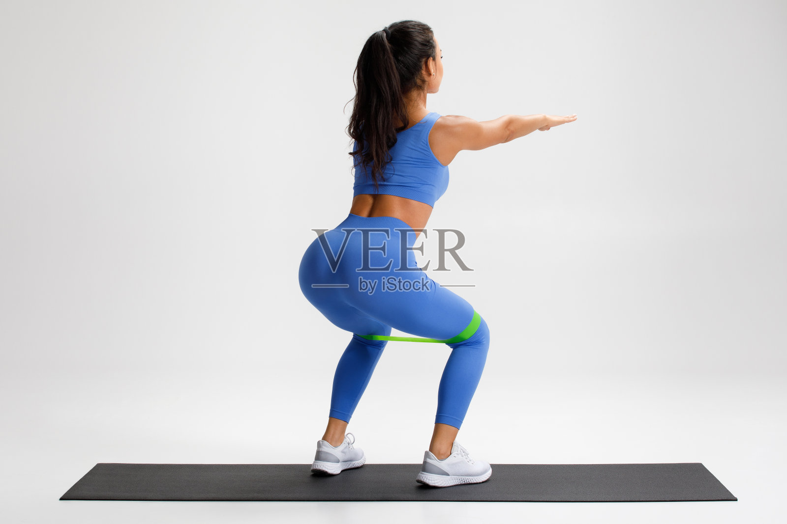 健身女性做深蹲运动臀部与阻力带在灰色背景。运动女孩健身照片摄影图片