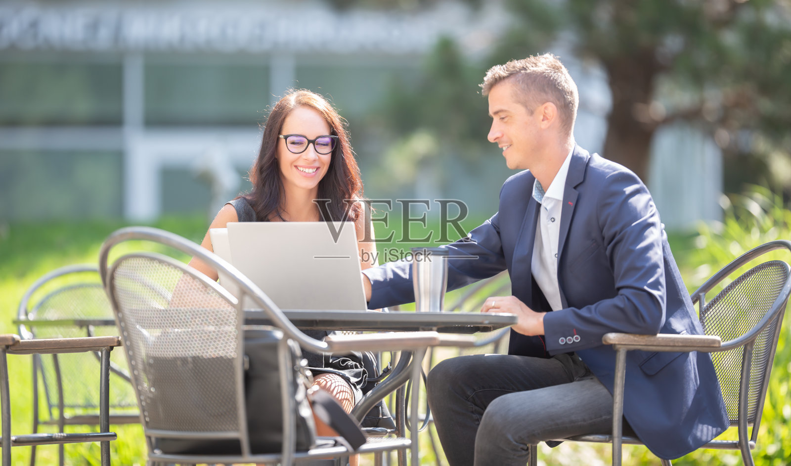 办公室男女同事在户外打开笔记本电脑和外卖咖啡杯讨论工作。照片摄影图片