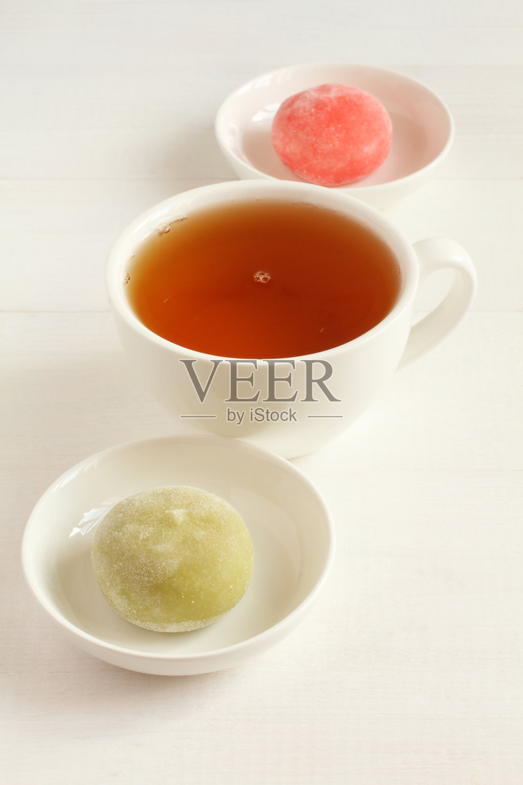 两种日式点心麻糬——蜂蜜石榴和绿色抹茶放在白色的小碗里，一杯绿茶放在白色的木桌上。特写镜头照片摄影图片