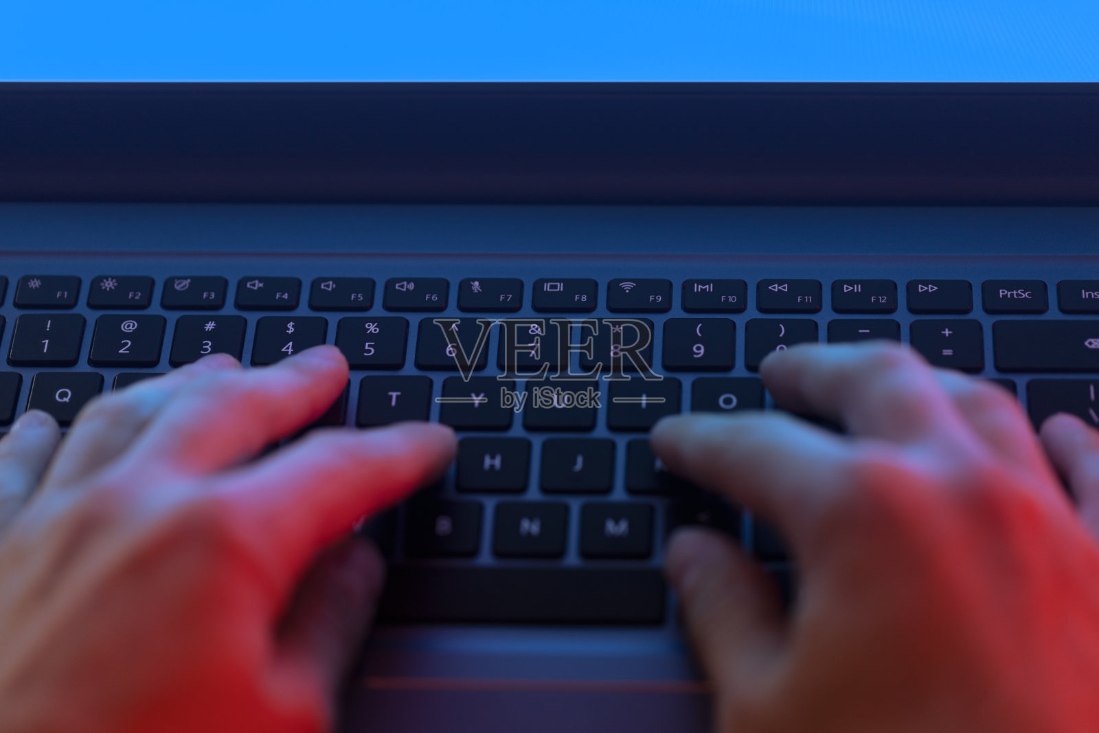 一名男子在黑暗中使用笔记本电脑，屏幕发出蓝色的光芒照片摄影图片