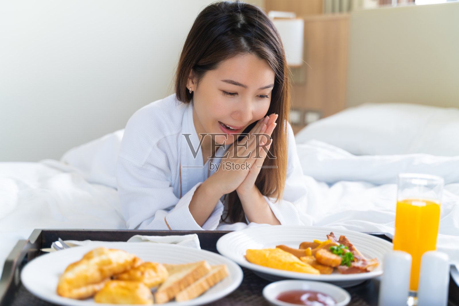 画像美丽的年轻亚洲女人穿着浴袍享受早餐在卧室的床上照片摄影图片