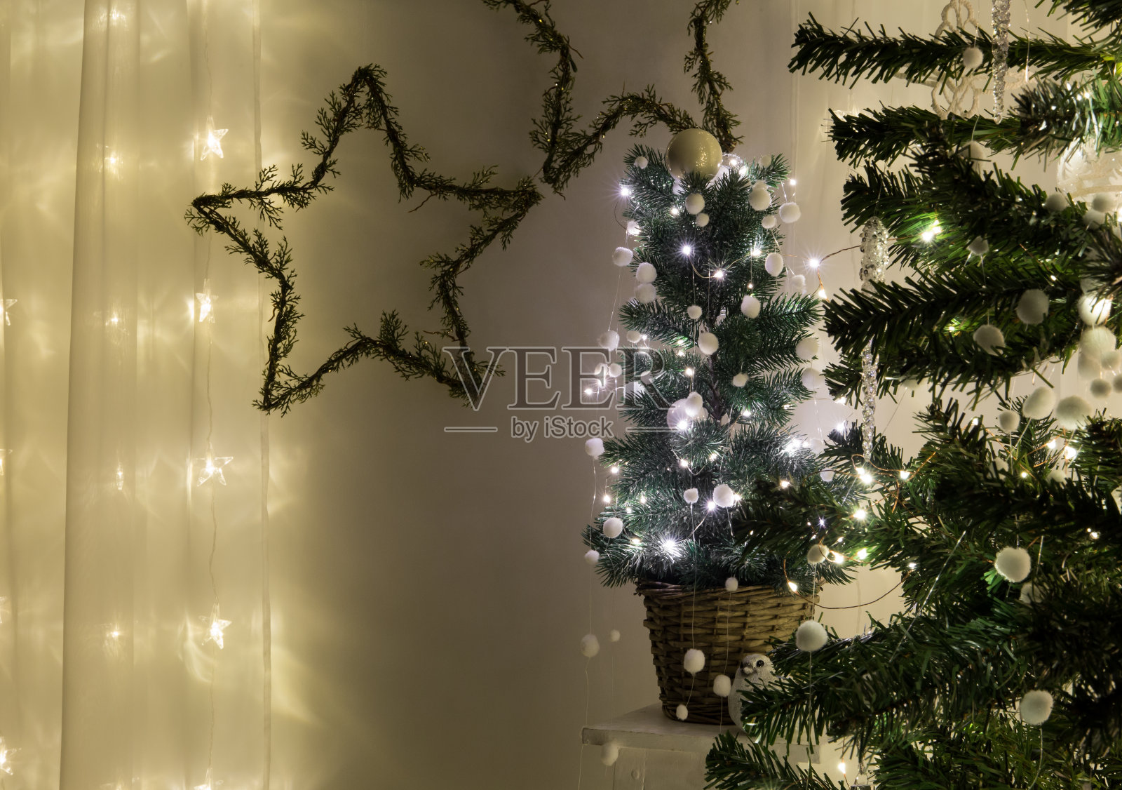 可爱的盆栽圣诞树装饰着金属丝微型led灯和白色的小装饰球、球、球或毛毡球花环在夜间室内。墙上的星形花环。文本的空间。照片摄影图片