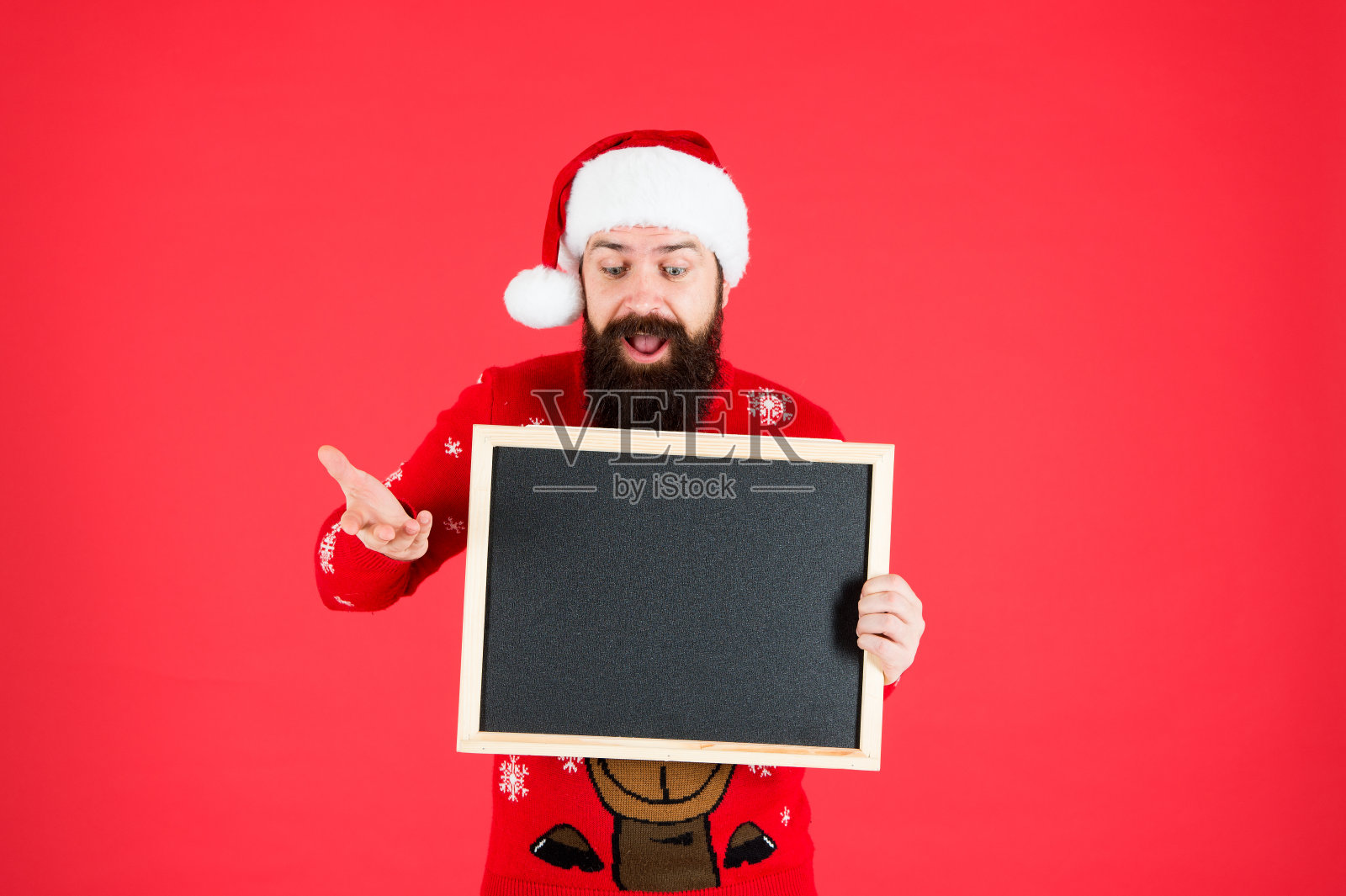 难以置信。有广告的圣诞老人帽子。黑板上的信息。男子手持空白黑板抄写空间。圣诞老人红色背景。冬天的公告。冬天的事件。寒假照片摄影图片
