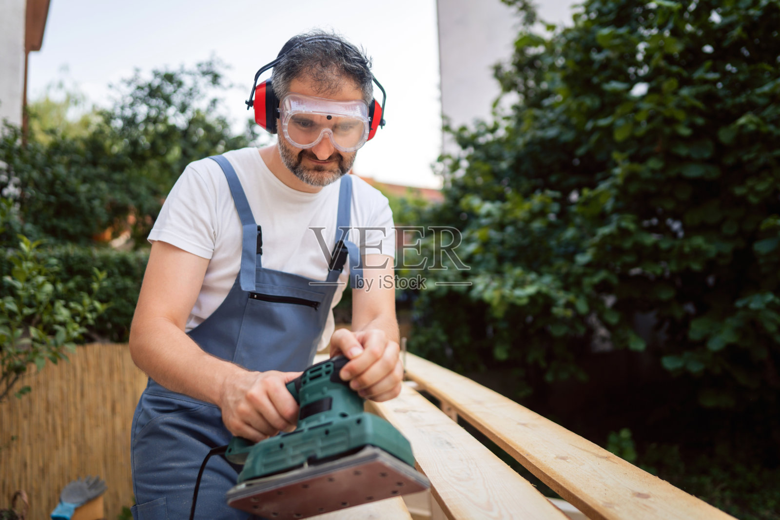 在戴着护目镜和护耳的同时，木工用砂光机工作照片摄影图片