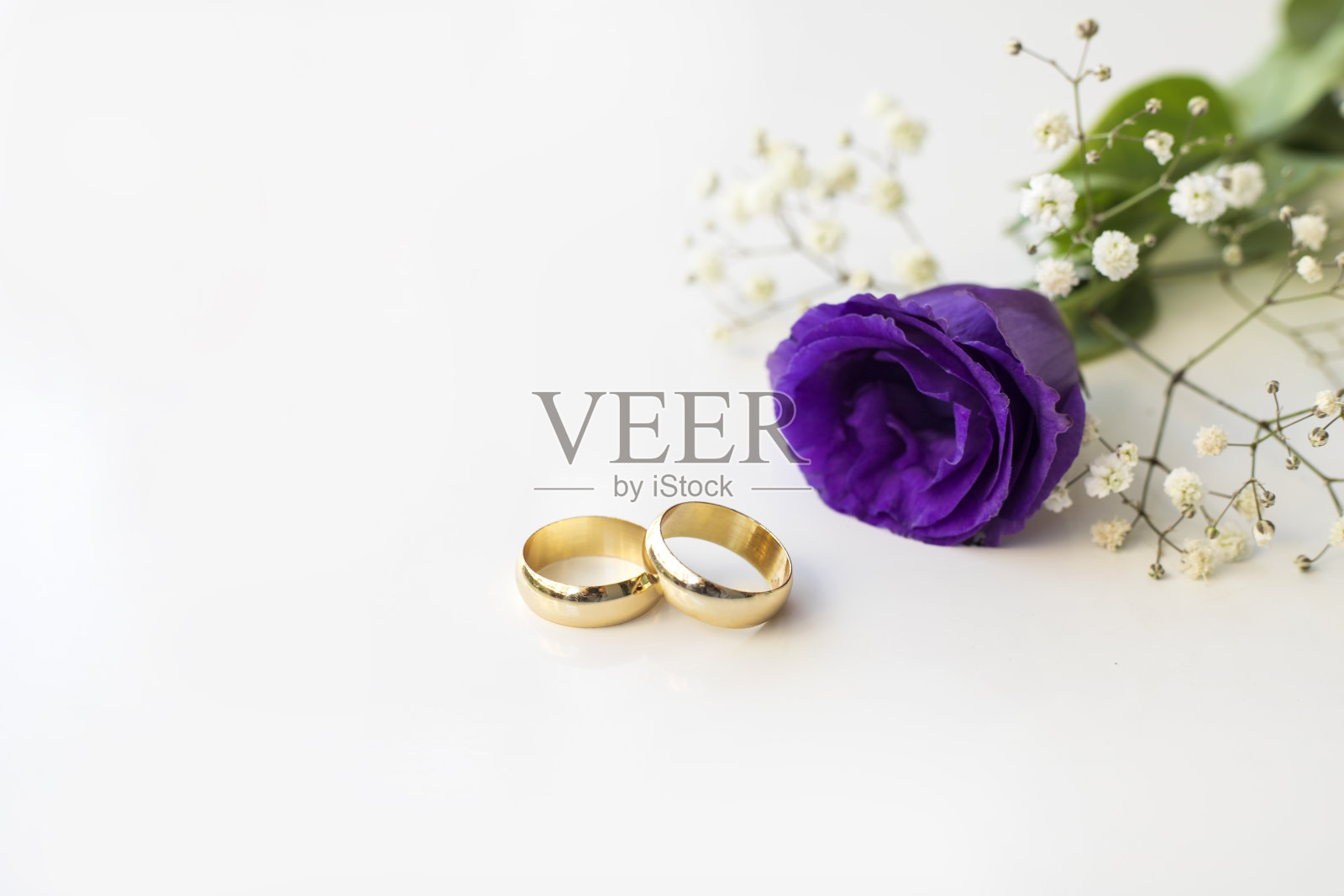白色背景上有紫色的花和两枚金色的结婚戒指。照片摄影图片