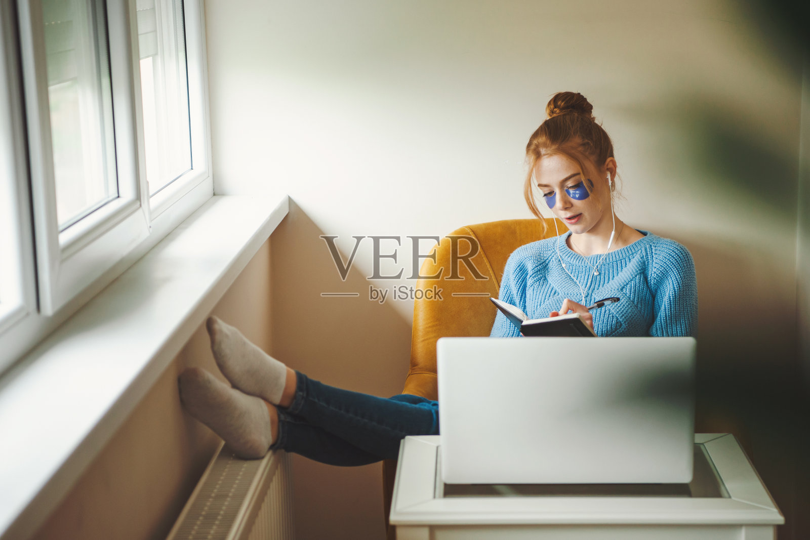 一名年轻女子坐在扶手椅上，坐在电脑前学习，一边做笔记，一边听音乐照片摄影图片