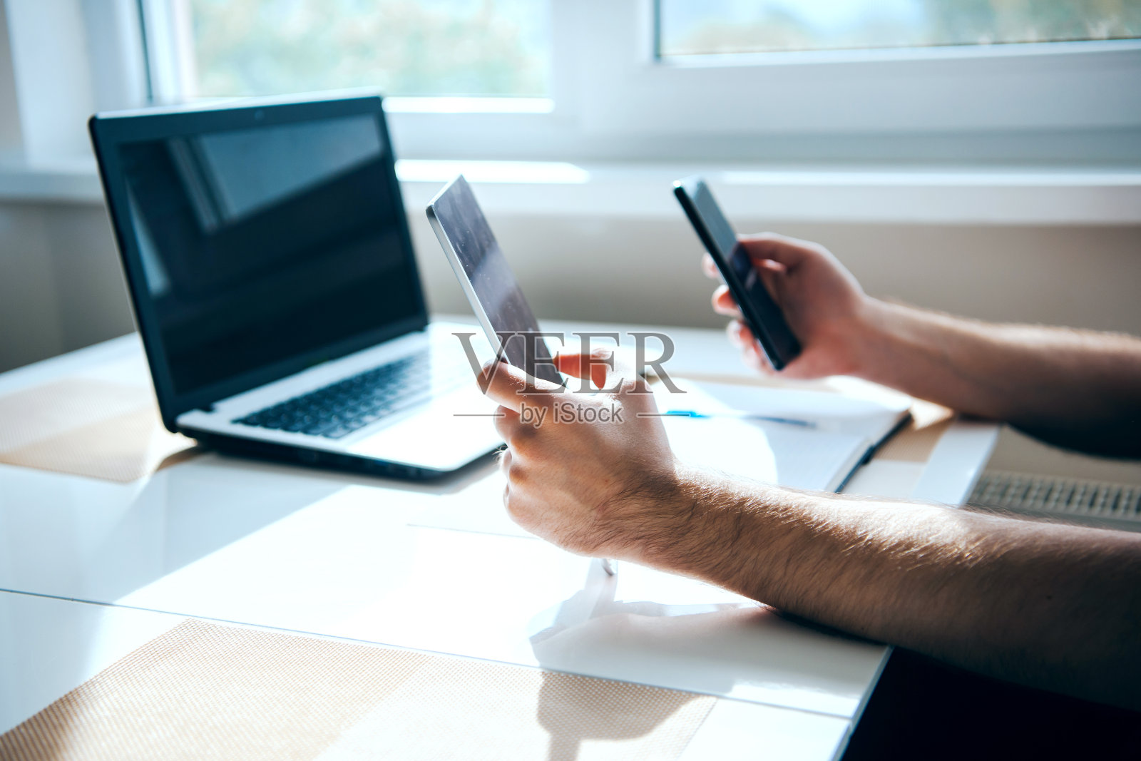 男人的手拿着两部手机和桌上的一台笔记本电脑。现代技术。从一个设备向另一个设备传送信息照片摄影图片