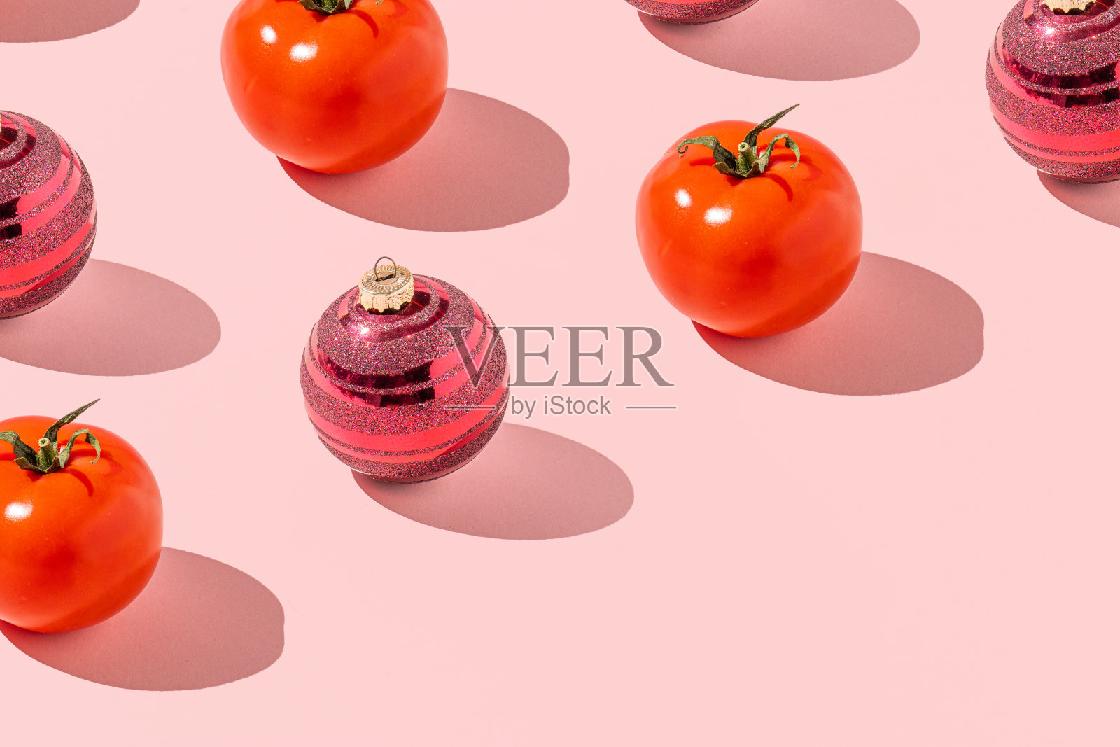 创意节日图案与新鲜西红柿和红色圣诞装饰物在粉红色的背景。新年的概念。照片摄影图片