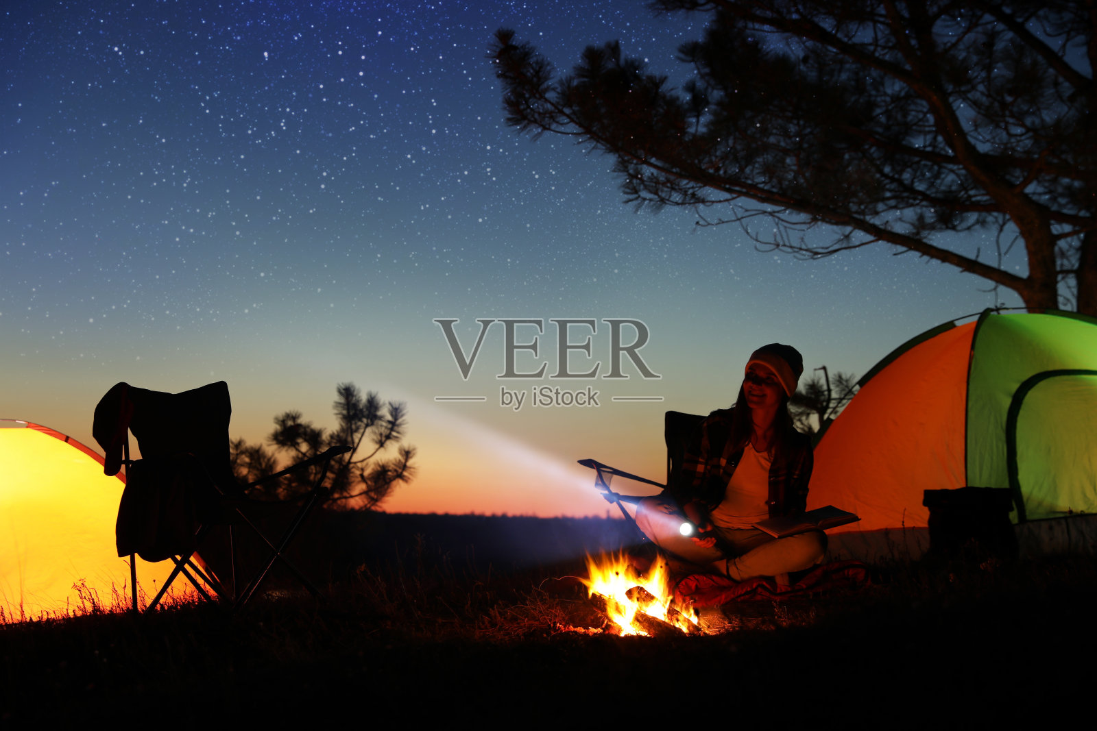 一个人的剪影在海滩的岸边，拿着啤酒，看着夜晚的地平线旁边的帐篷照片摄影图片_ID:420713188-Veer图库
