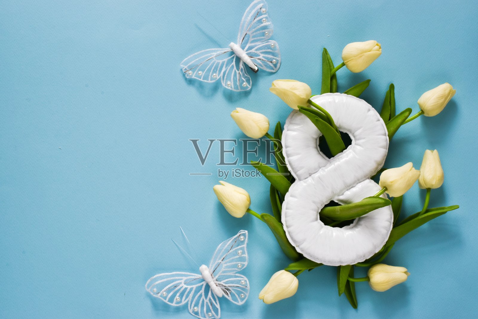 三八国际妇女节贺卡。白色郁金香，蝴蝶和白色数字8浅蓝色背景。复制空间，平铺。节日的概念照片摄影图片