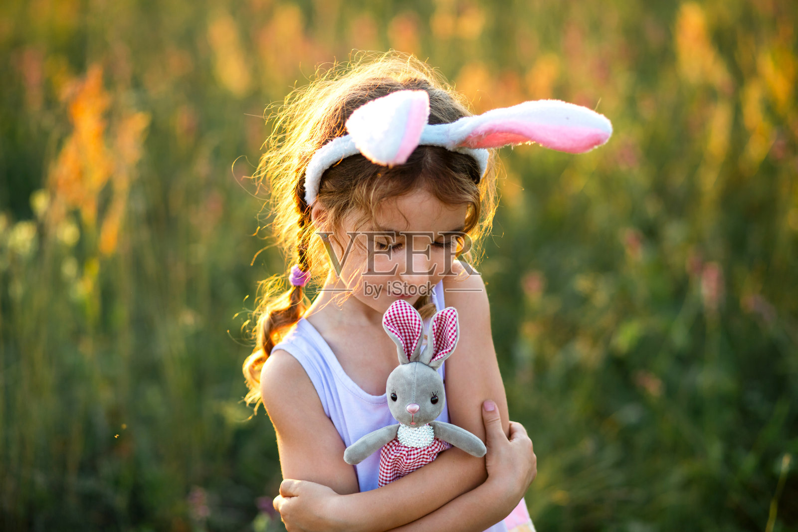 可爱的5岁小女孩，长着兔耳朵，温柔地抱着一只玩具兔子。复活节，复活节兔子，童年，快乐的孩子，春天。照片摄影图片