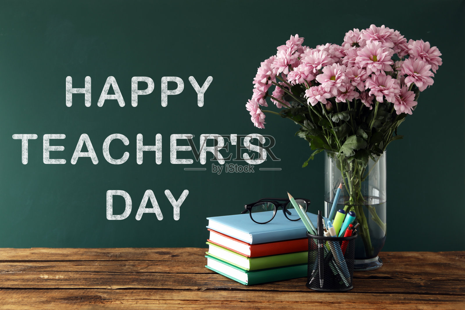 在桌子旁的绿色黑板上写上“教师节快乐”，并放上文具和花束照片摄影图片