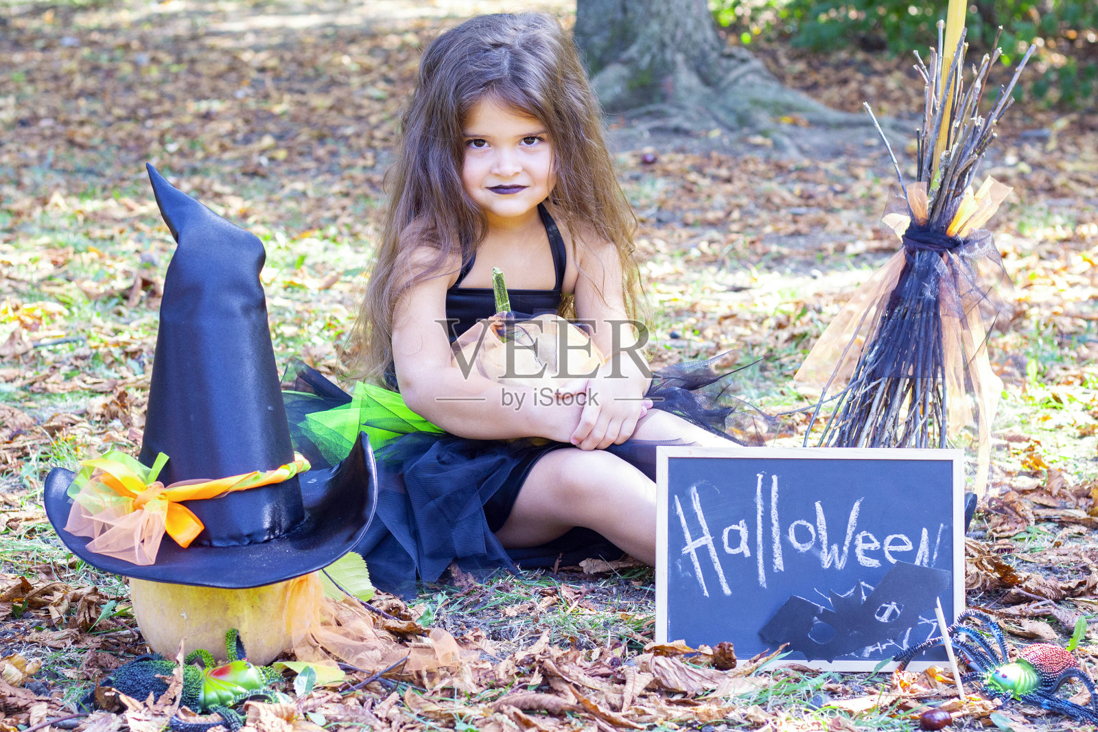 万圣节穿着女巫服装的女孩。贴着标语:万圣节。女孩坐在草地上照片摄影图片