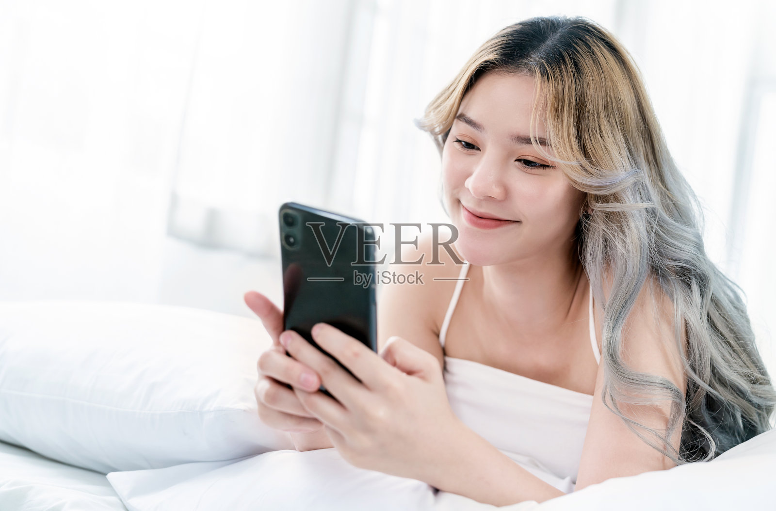 年轻美丽的亚洲女性肖像放松使用智能手机小工具在卧室。微笑快乐的亚洲女孩网上购物工作从家里。教育、电子商务、自由职业技术连接亚洲人照片摄影图片