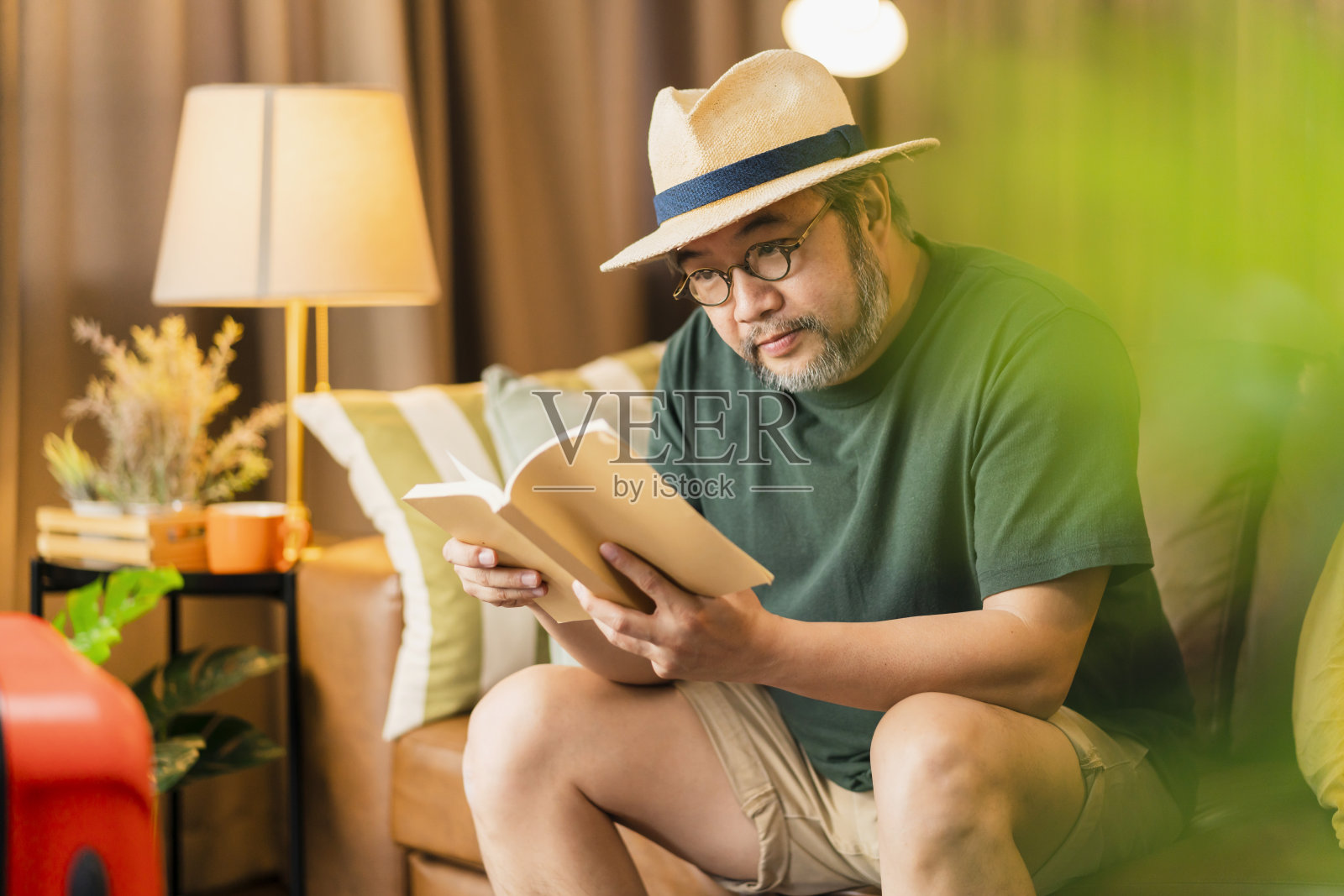 准备出国旅游的亚洲成年男性男士休闲布衣坐在沙发沙发旁边的行李旅行袋，手拿着书在酒店大堂等候照片摄影图片