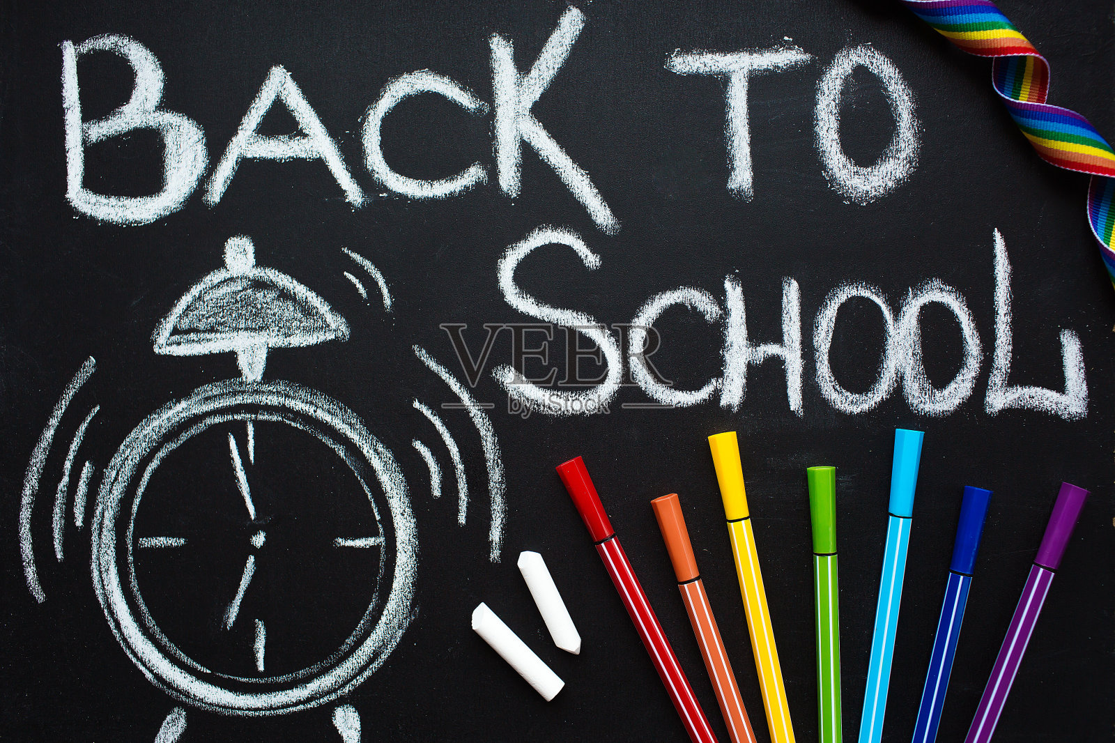 学校用品，闹钟，白色粉笔在黑板上写着:“回到学校”和彩色钢笔。一张平床的俯视图。新学年的概念。照片摄影图片