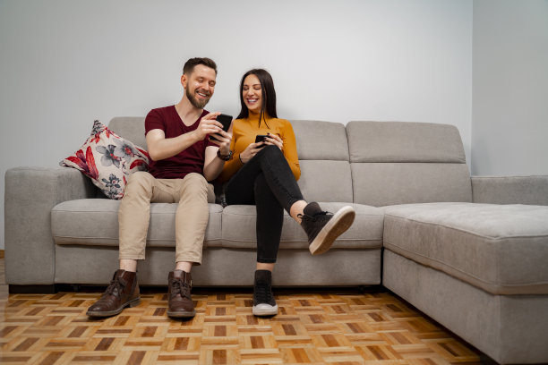 一对年轻夫妇坐在沙发上玩智能手机图片下载